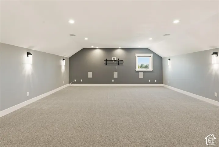 Spacious room featuring sloped ceilings, recessed lighting, wall sconces, built-in speakers, and light-toned carpeting