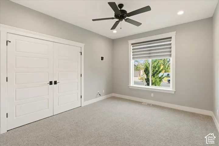 Bright room featuring a large window with horizontal blinds, overhead ceiling fan, recessed lighting, double panel doors with matte black hardware, and gray carpet flooring