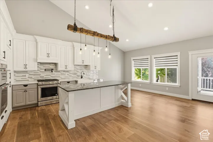 Spacious kitchen featuring white cabinetry, stainless steel appliances, a textured tile backsplash, and a central island with a dark countertop