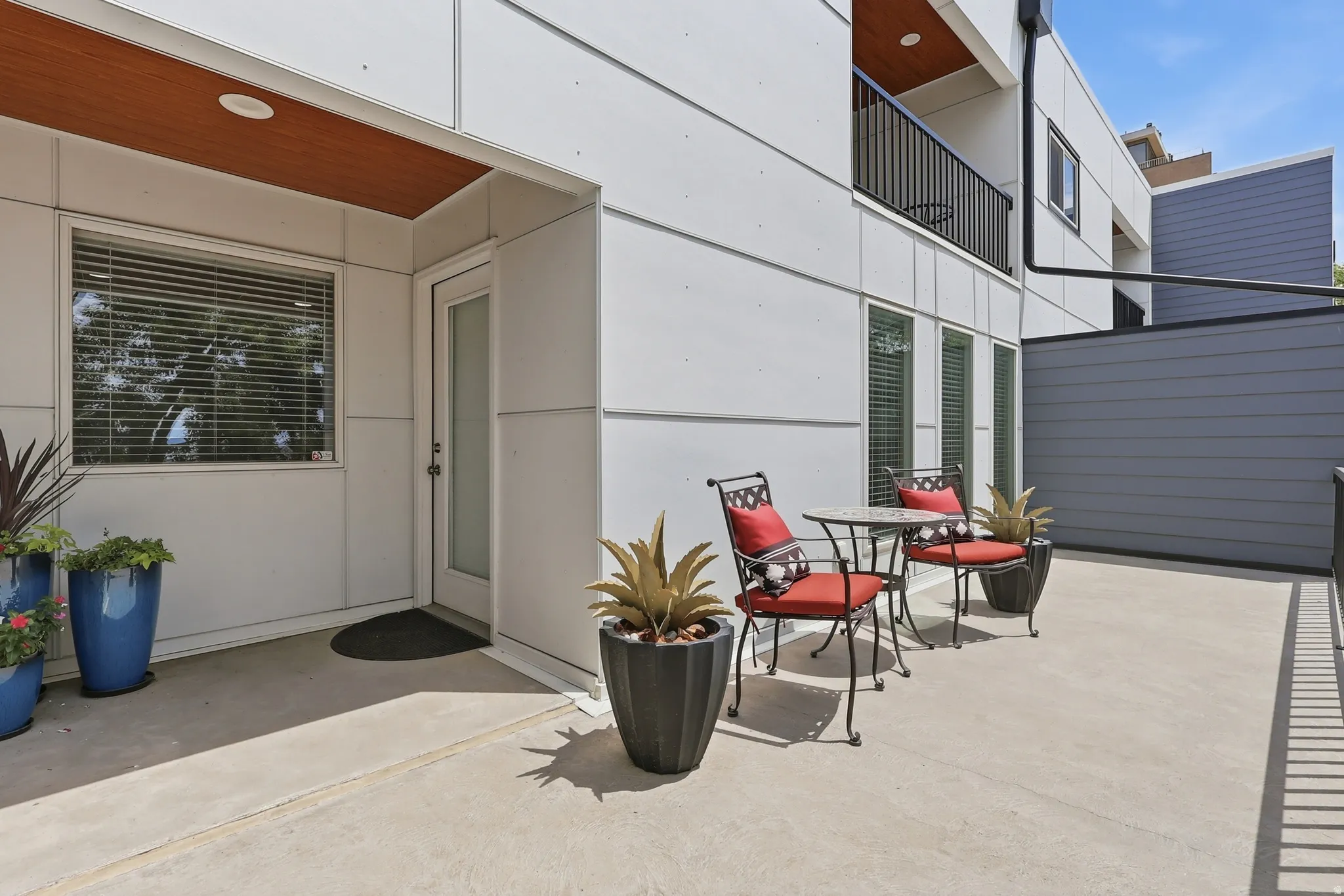 Spacious concrete patio featuring a privacy fence, contemporary exterior paneling, wood-finish soffit, and a glass-paneled entry door