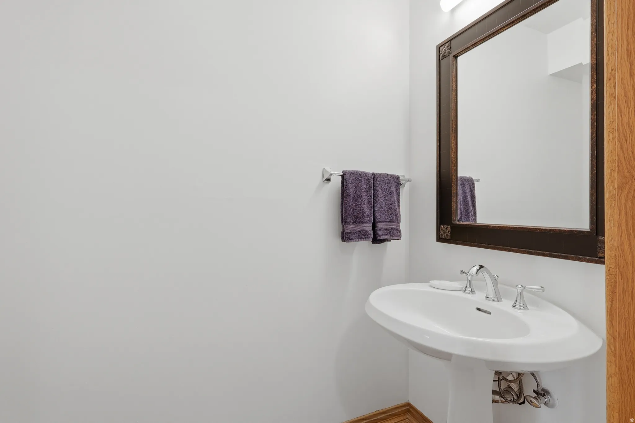 Pedestal sink with chrome faucet, framed mirror, and wall-mounted light fixture