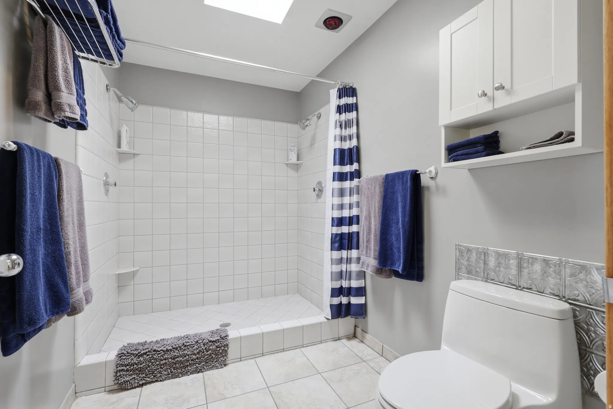 Primary suite bathroom featuring a large, white subway-tiled double-headed shower with integrated corner shelves.