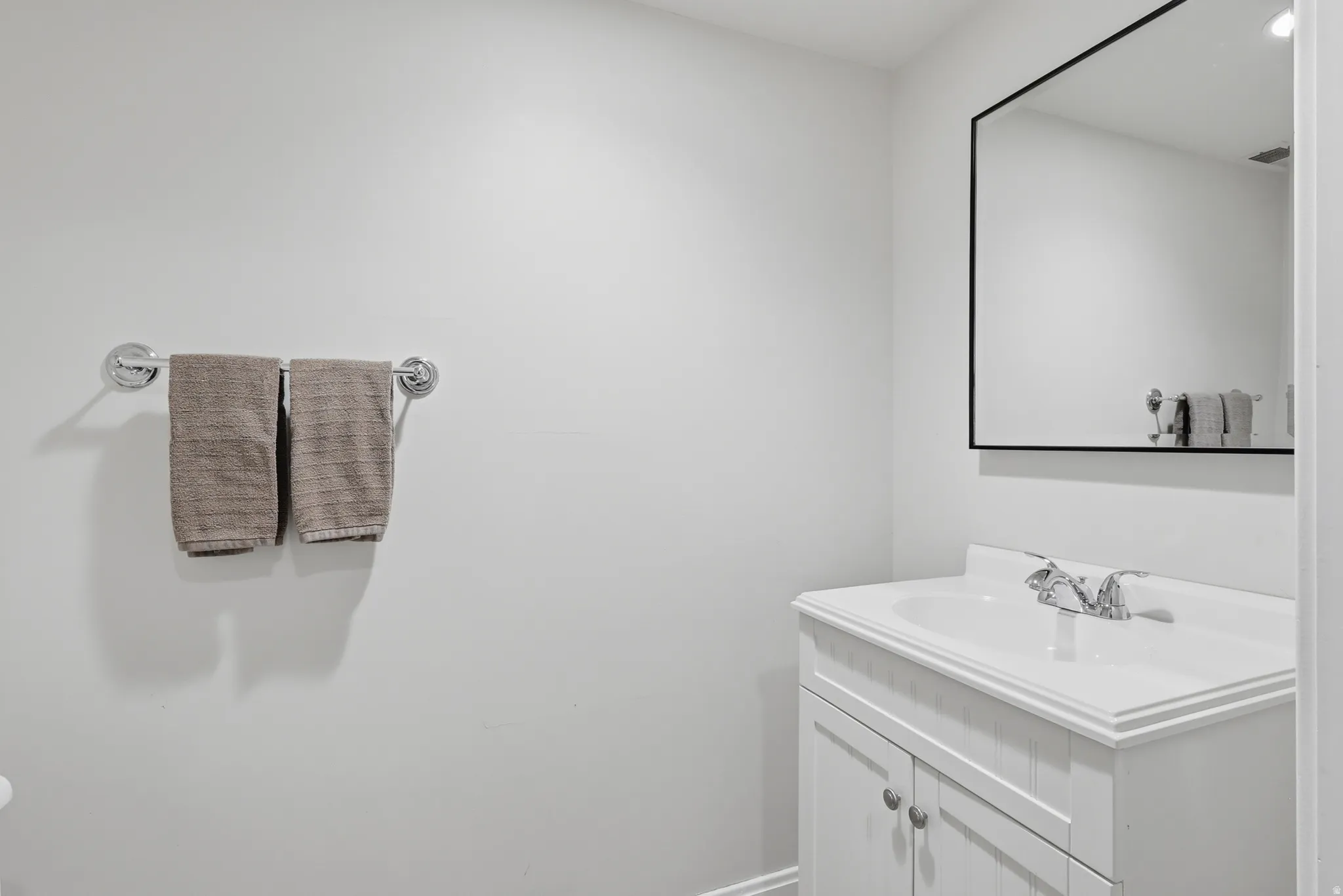 Bathroom vanity with a white countertop and integrated sink, and a wall-mounted mirror with a black frame