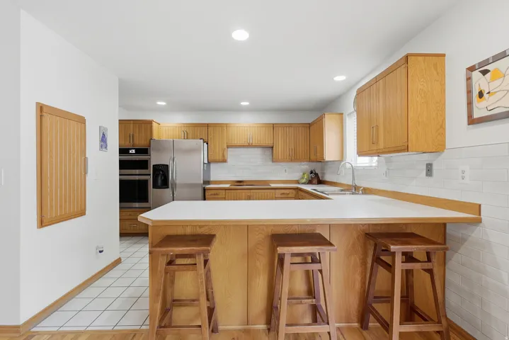 Kitchen featuring light wood cabinetry, white subway tile backsplash, stainless steel appliances, a double basin sink, and a peninsula with a white countertop