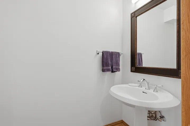 Pedestal sink with chrome faucet, framed mirror, and wall-mounted light fixture