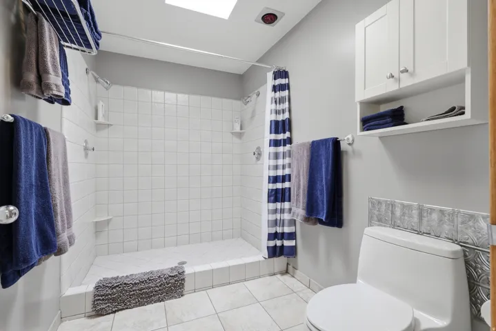 Primary suite bathroom featuring a large, white subway-tiled double-headed shower with integrated corner shelves.