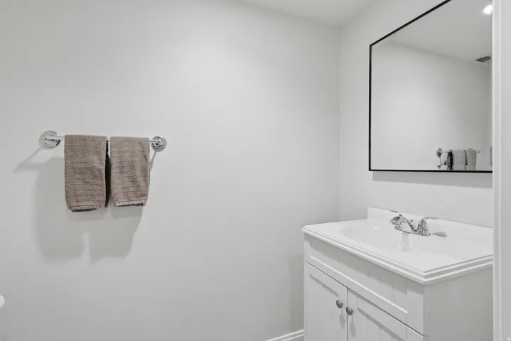 Bathroom vanity with a white countertop and integrated sink, and a wall-mounted mirror with a black frame