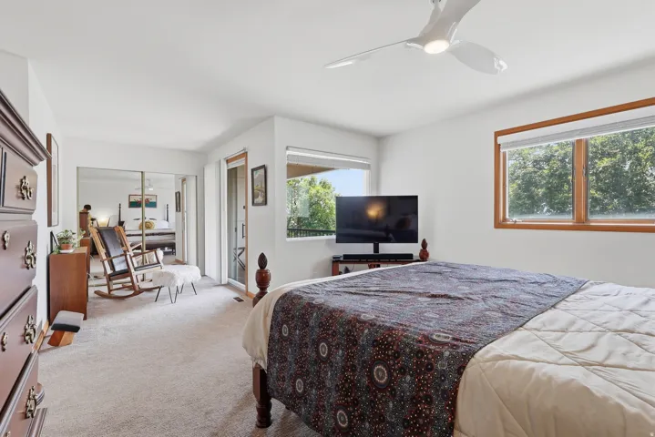 Primary suite featuring a ceiling fan, wood-framed windows, and a flex space with a sliding glass door leading to a private view deck.