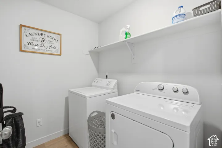 Dedicated laundry area featuring light wood-finish flooring and crisp white walls