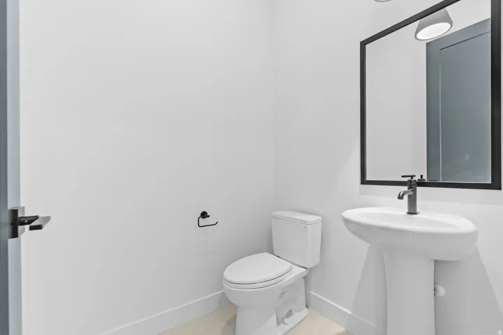 Contemporary pedestal sink with a matte black faucet, complemented by a rectangular framed mirror