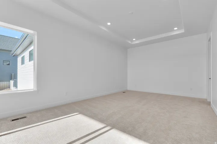 Spacious room featuring neutral carpeting, a large window, recessed lighting, and a tray ceiling