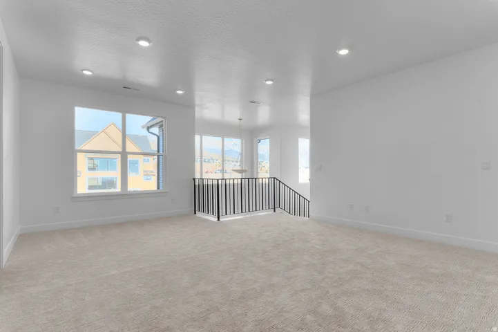 Spacious room with plush carpeting, multiple windows providing natural light, recessed lighting, and a modern black metal railing