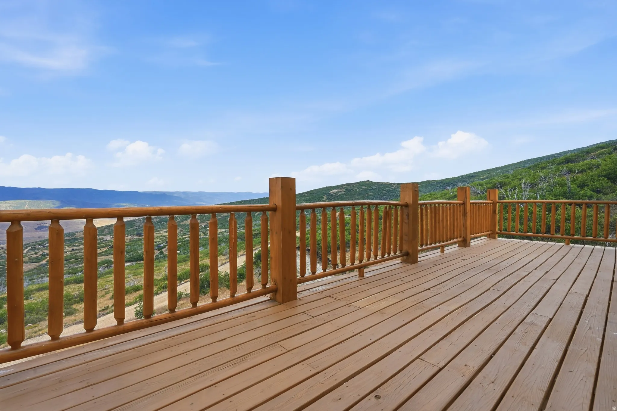 Expansive wooden deck with natural wood railing and balusters, featuring open-air exposure and a mountainous landscape