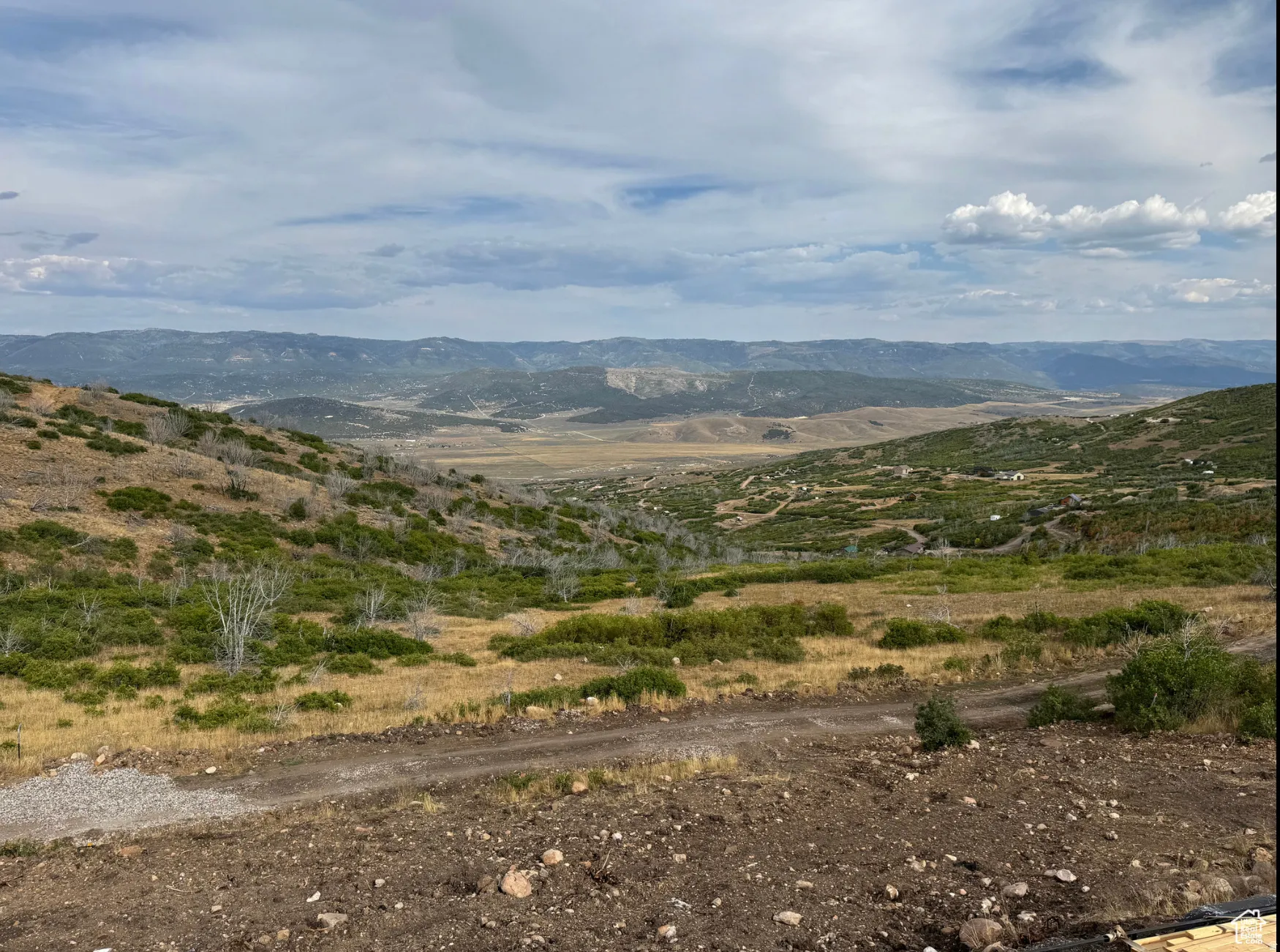 Expansive mountain landscape featuring varied terrain and distant mountain ranges under a partly cloudy sky
