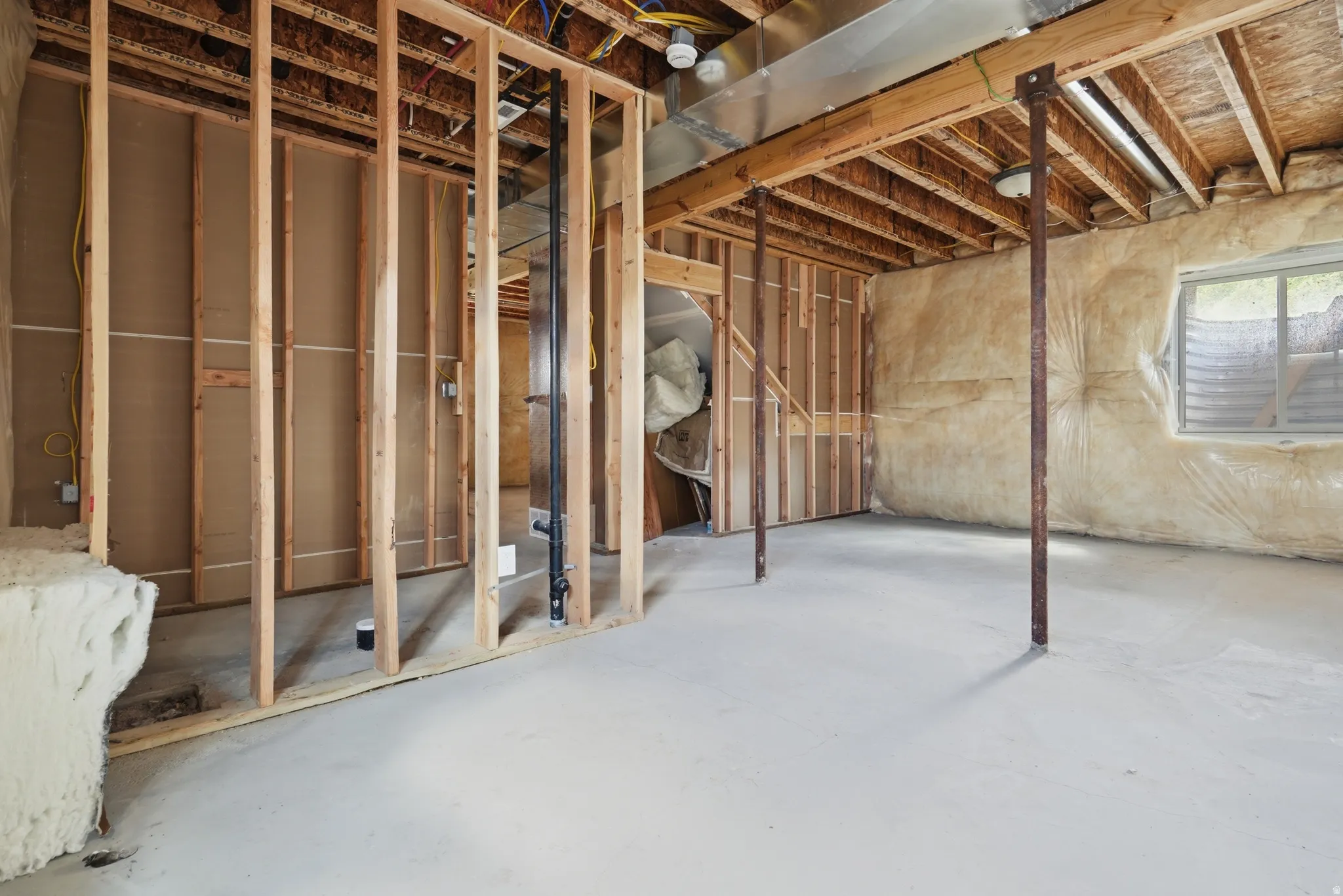 Unfinished basement featuring wood framing, exposed joists, concrete flooring, and a visible window opening