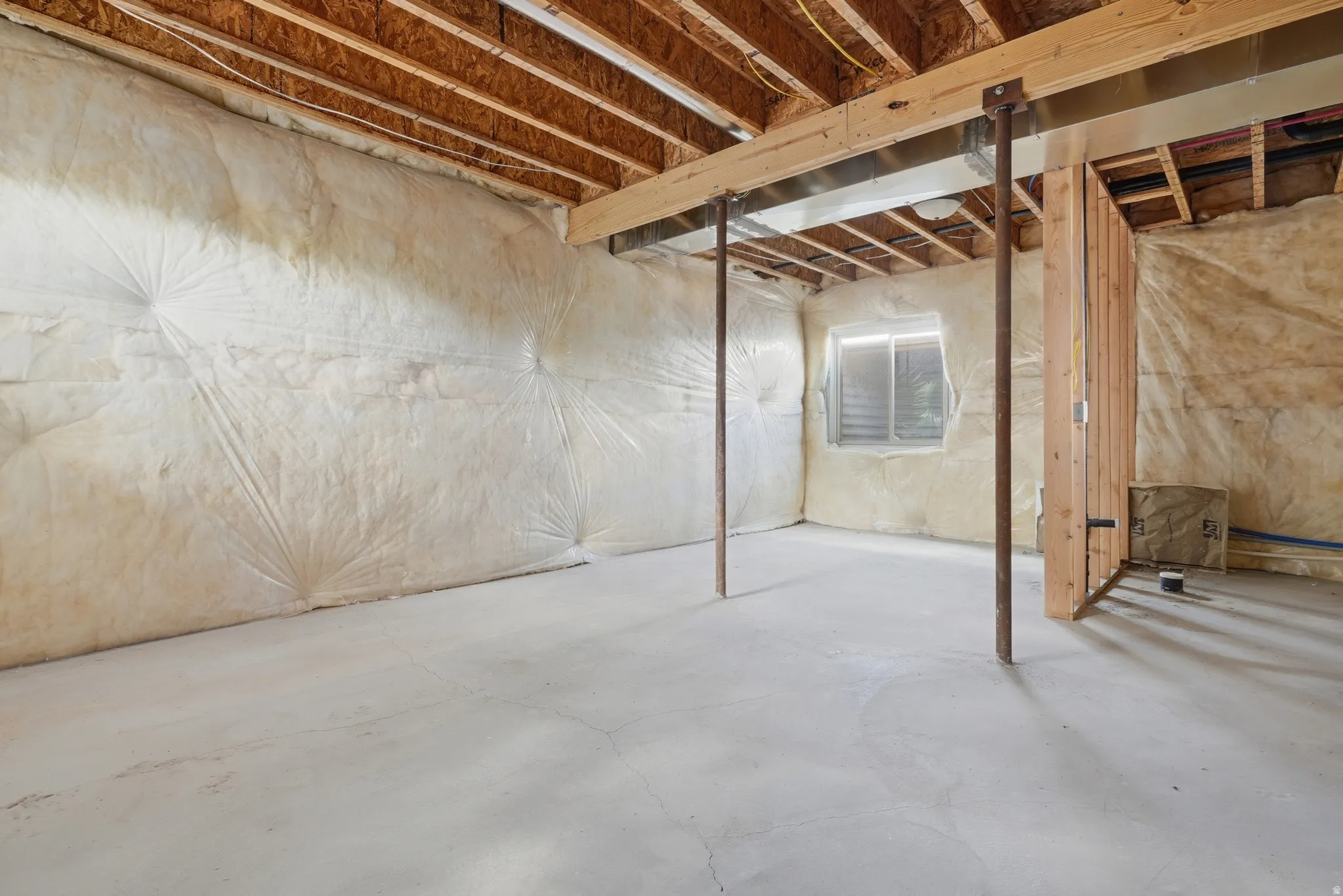Unfinished basement offering exposed wood ceiling joists, concrete flooring, and insulated walls