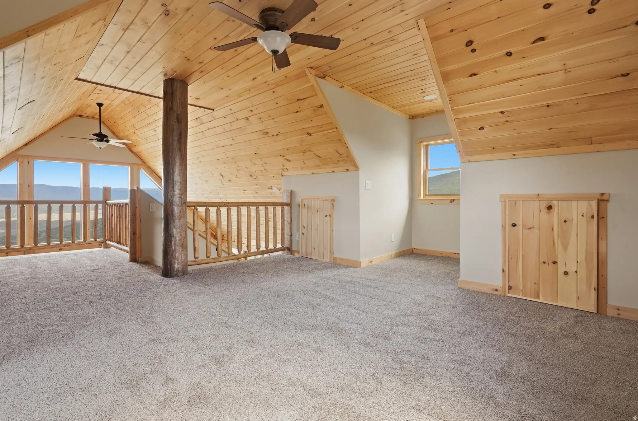 Spacious loft area featuring a natural wood plank ceiling, light gray carpet flooring, and a log support beam