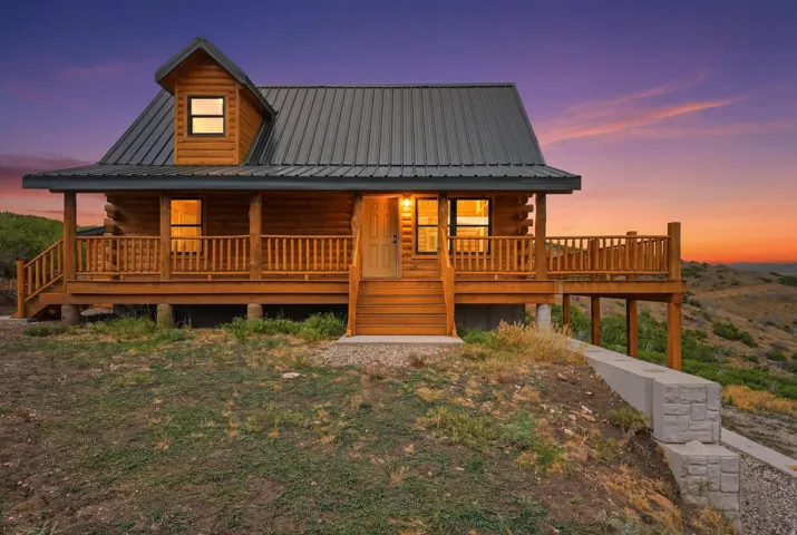 Log cabin exterior featuring a covered porch with wood railings, a metal roof, and a dormer window