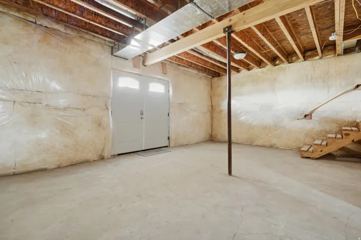Concrete floor basement with exposed wood joists and a double door exterior access