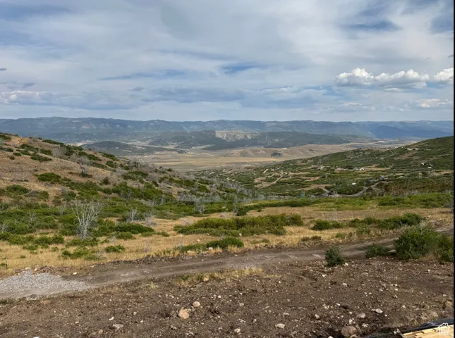 Expansive mountain landscape featuring varied terrain and distant mountain ranges under a partly cloudy sky