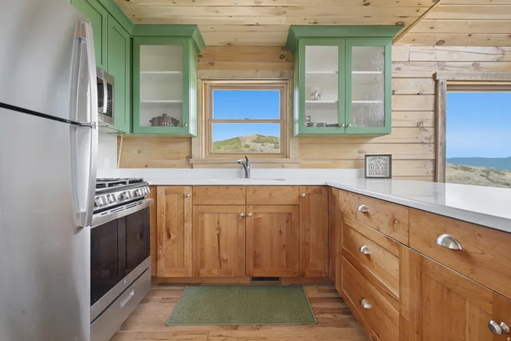 Kitchen featuring natural wood cabinetry, light green upper cabinets with glass fronts, and white countertops