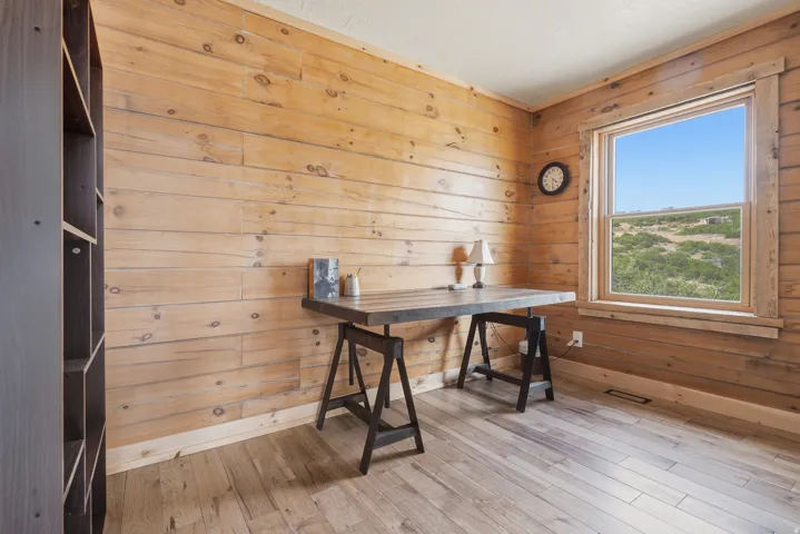 Wood-paneled room featuring wood-finish flooring, a large window with wood trim, and a built-in dark wood shelving unit