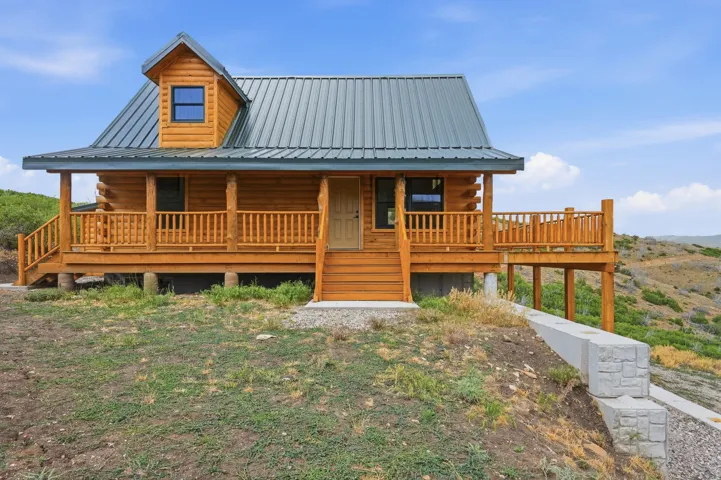 Log home featuring a covered front porch with wood railings and steps, a dormer window, and a metal roof