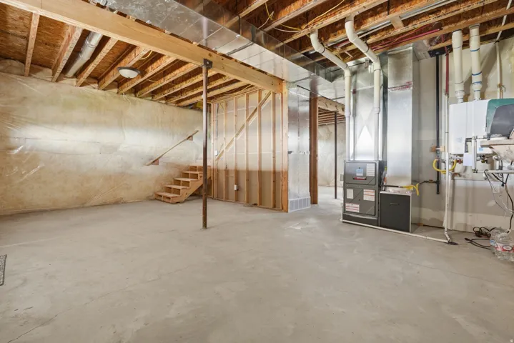 Spacious unfinished basement offering concrete flooring, exposed wood framing, and utility hookups
