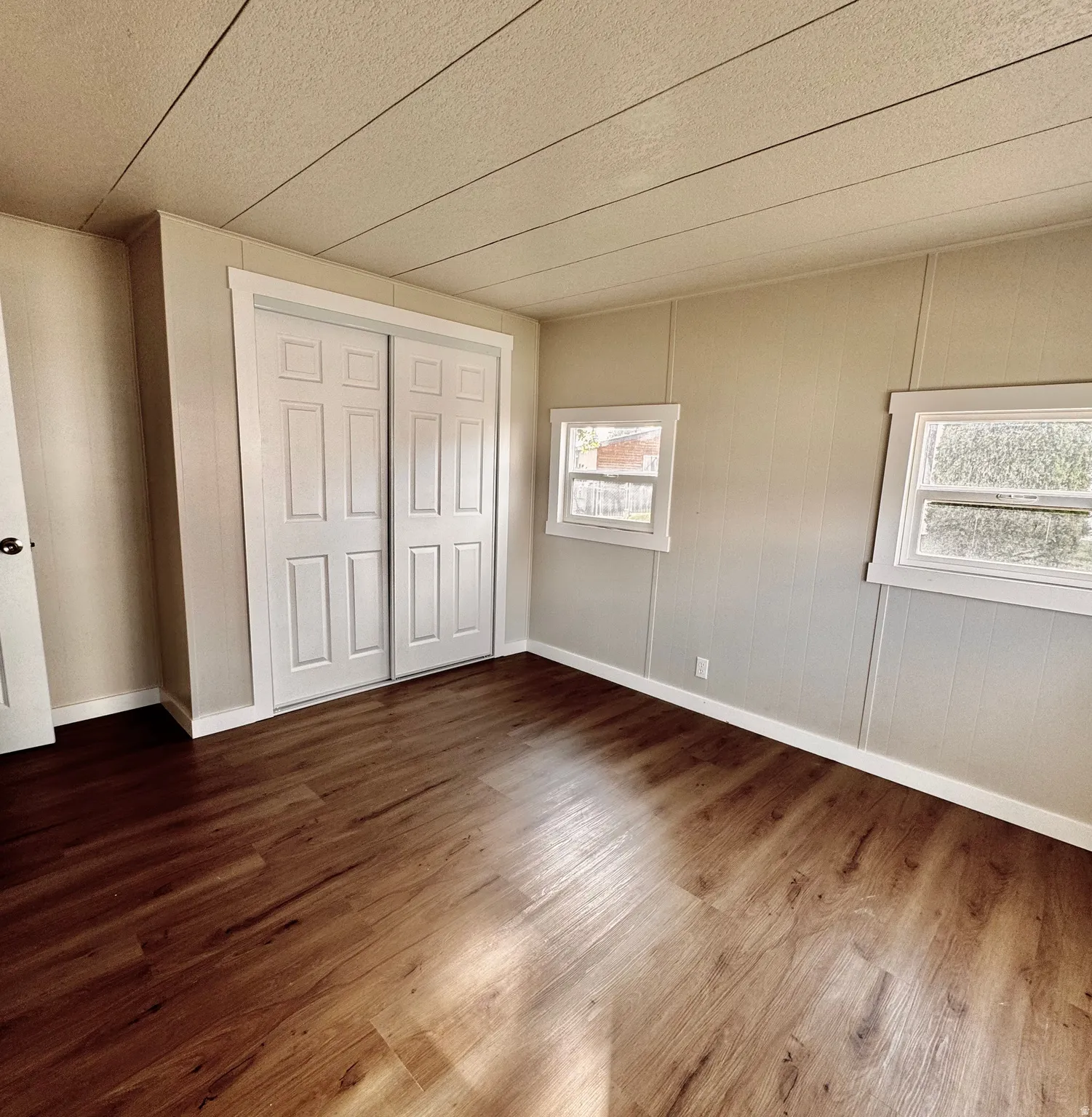 Interior room featuring wood-finish flooring, two large sliding closet doors with paneled detailing, and two windows providing natural illumination