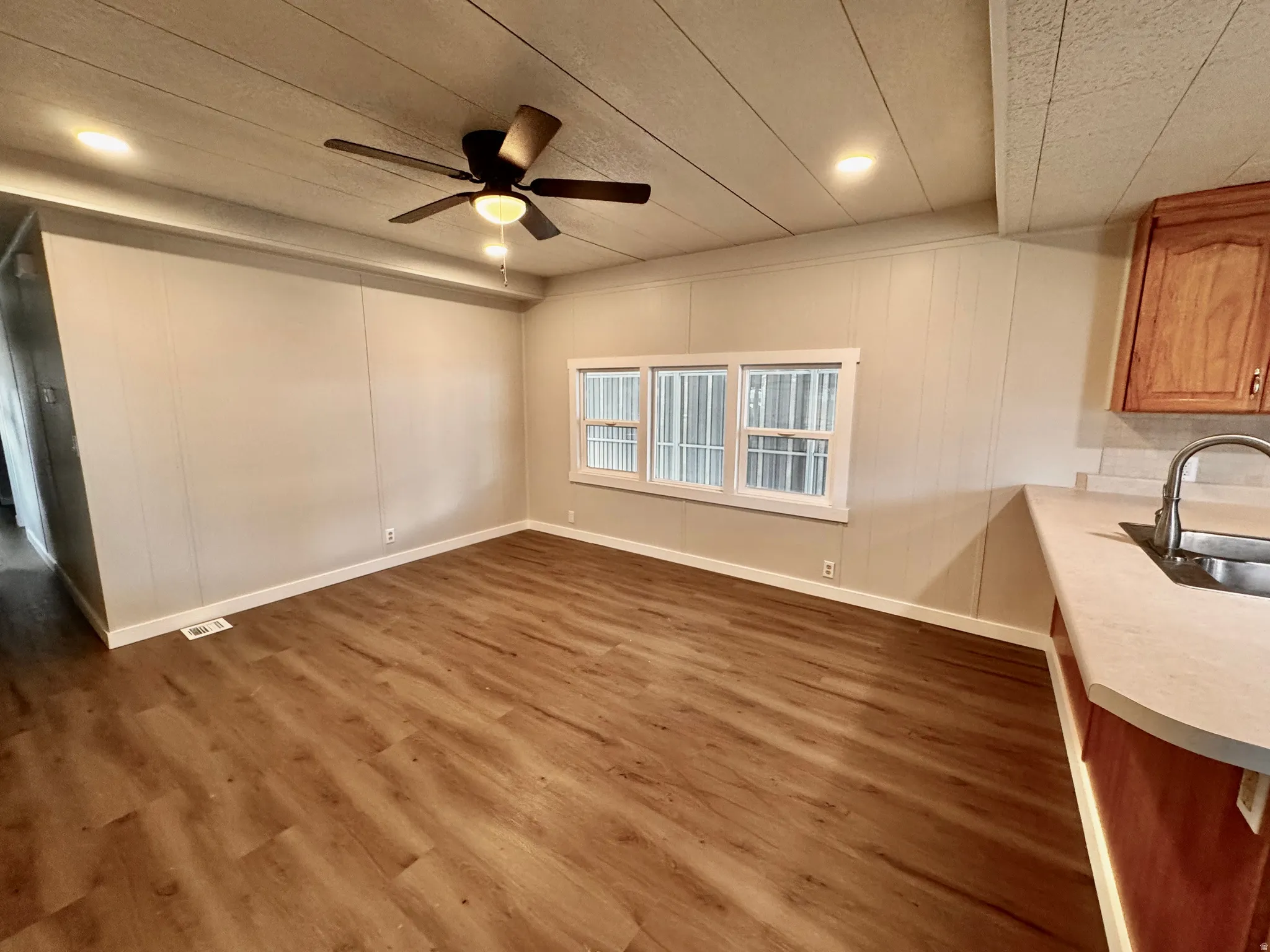 Open concept living area featuring wood-finish flooring, a ceiling fan with integrated lighting, recessed lighting, and a window with white trim
