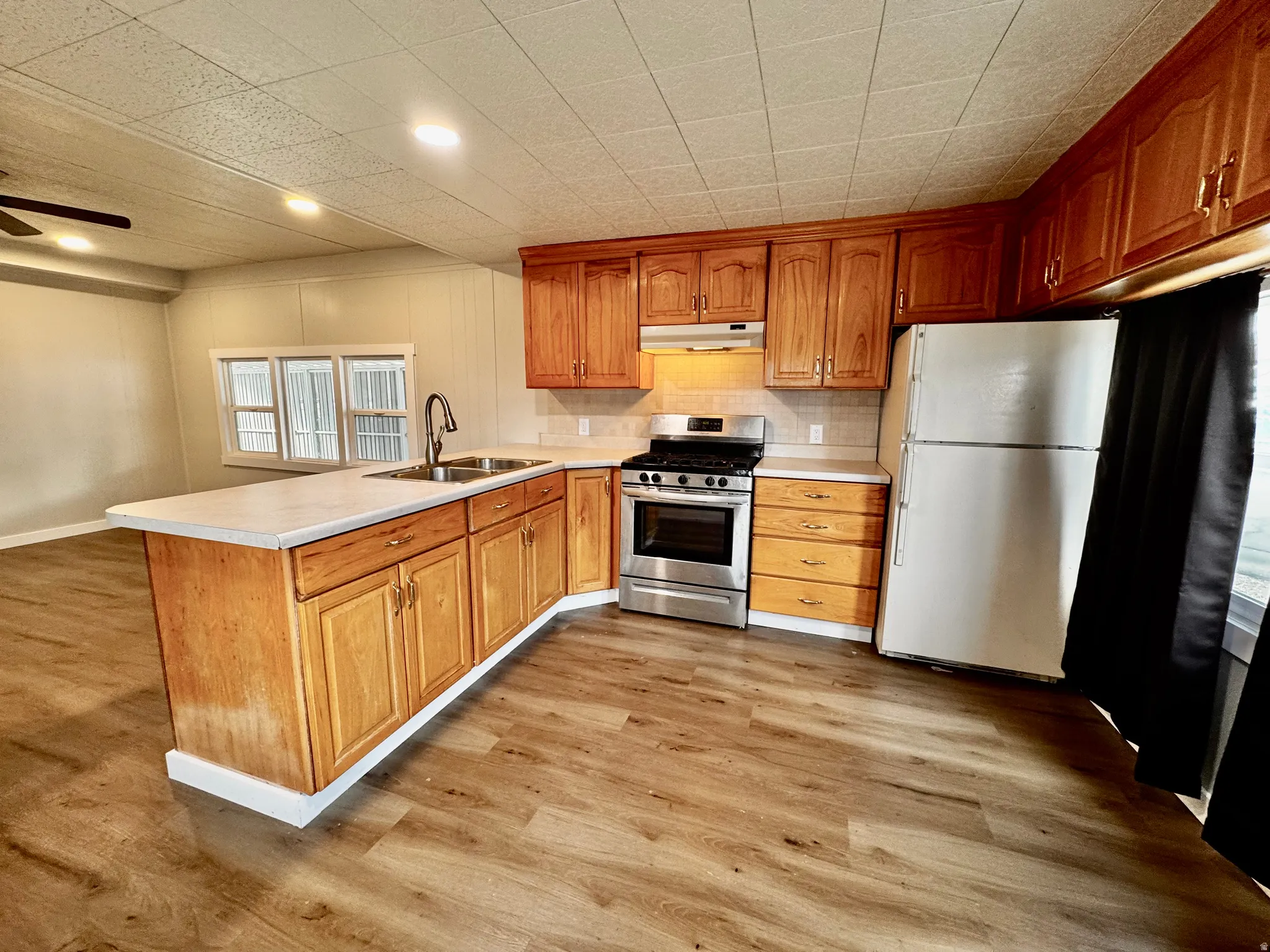 Kitchen featuring wood-finish flooring, wood cabinetry, light-colored countertops, a stainless steel range, and a dual basin sink with a gooseneck faucet