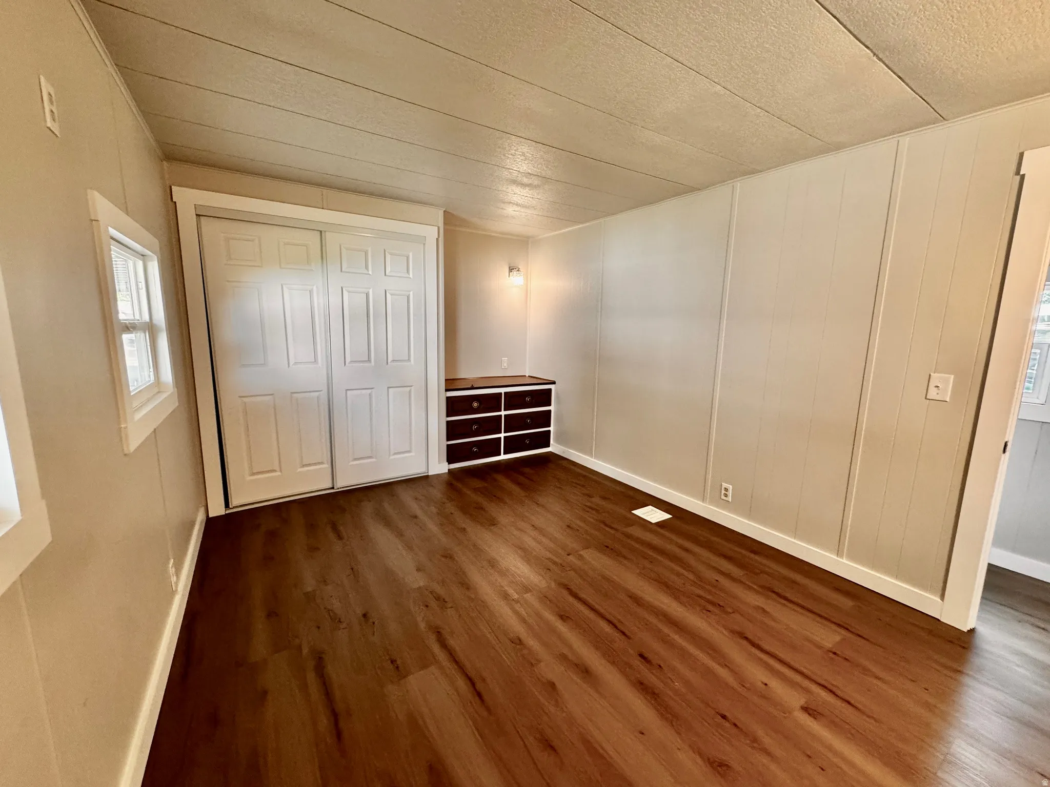 Spacious room featuring wood-finish flooring, light-toned vertical paneling, and a built-in storage unit with dark wood-finish drawers