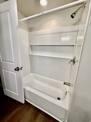 Bathtub and shower combination featuring white subway tile surround, built-in shelving, a brushed nickel shower head, and coordinating faucet hardware