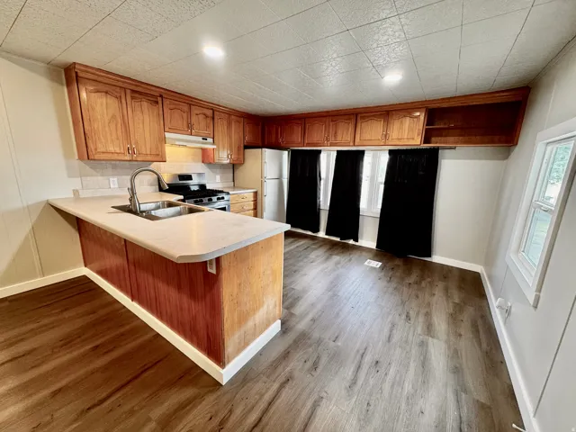 Kitchen featuring wood cabinetry, laminate countertops, a stainless steel sink with a gooseneck faucet, a gas range, and wood-finish flooring