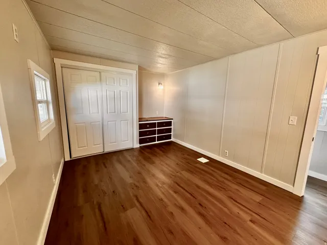 Spacious room featuring wood-finish flooring, light-toned vertical paneling, and a built-in storage unit with dark wood-finish drawers