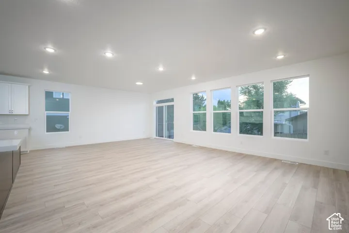 Open-concept living area featuring light wood-finish flooring, recessed lighting, and a wall of four large windows providing abundant natural light