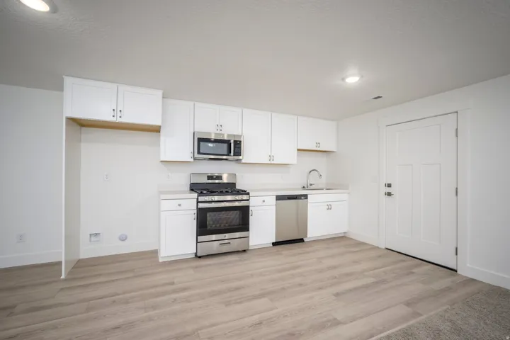 Kitchenette featuring wood-finish flooring, white cabinetry, and stainless steel appliances