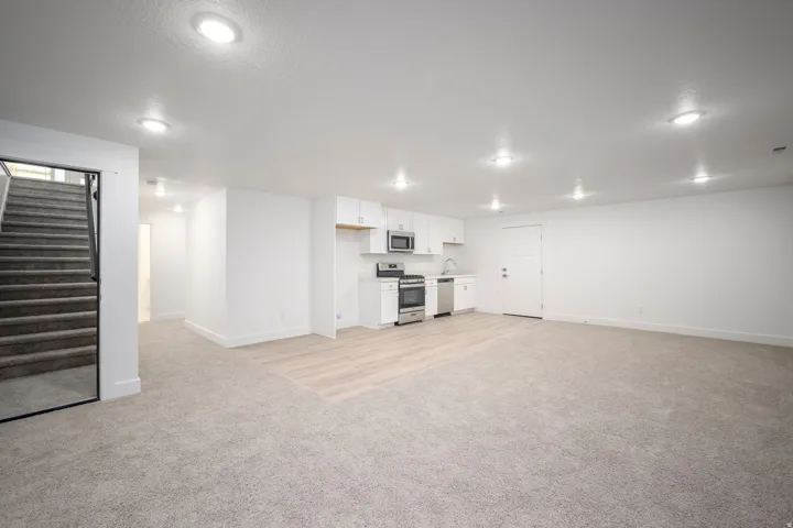 Spacious open-concept room featuring a functional kitchen area with white cabinetry, stainless steel appliances, and a light wood-finish flooring section