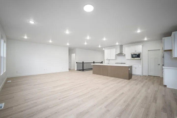 Open-concept living space featuring wood-finish flooring, recessed lighting, and a kitchen with white cabinetry, a central island, and stainless steel appliances including a range hood and microwave