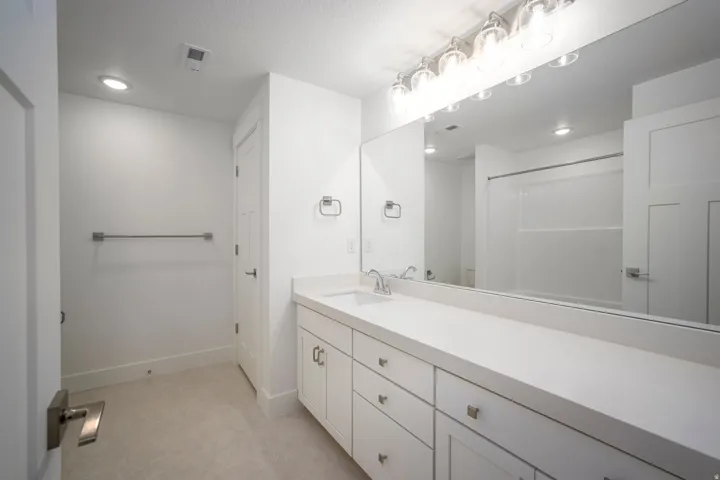 Bathroom featuring a dual vanity with white cabinetry and a light-toned countertop, a large wall-mounted mirror, and a multi-bulb vanity light fixture