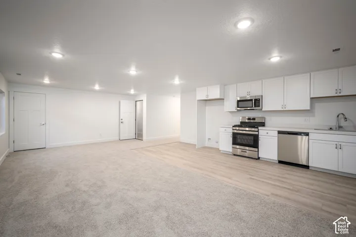 Open concept living area featuring a kitchen with white cabinetry and stainless steel appliances