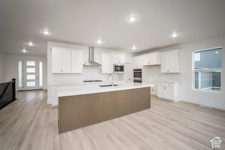 Open-concept kitchen featuring an expansive island with a contrasting wood-finish base, white cabinetry, integrated stainless steel appliances, and light-toned wood-finish flooring