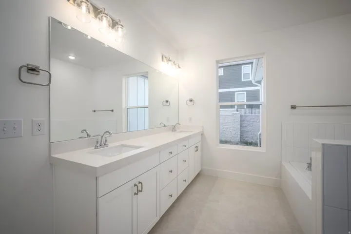Contemporary bathroom featuring a double vanity with white cabinetry, integrated sinks, a large mirror, and overhead vanity lighting