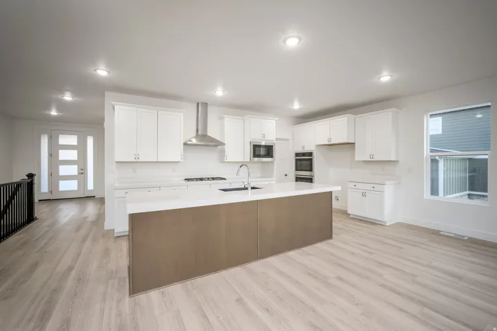 Open-concept kitchen featuring an expansive island with a contrasting wood-finish base, white cabinetry, integrated stainless steel appliances, and light-toned wood-finish flooring