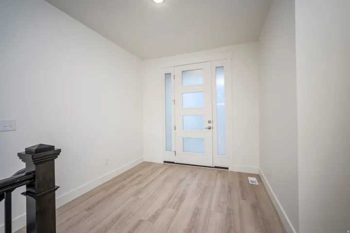 Entryway featuring a contemporary white door with frosted glass panels, an accompanying frosted glass sidelight, light wood-finish flooring, white baseboards, and a dark wood newel post