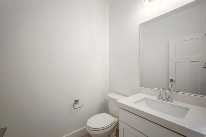 Bathroom featuring a white vanity with integrated sink, a large wall-mounted mirror, brushed nickel fixtures, a white toilet, and wood-finish flooring
