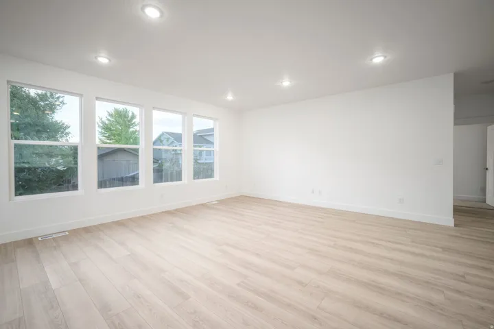 Spacious room featuring multiple large windows, recessed ceiling lighting, light wood-finish flooring, and crisp white walls