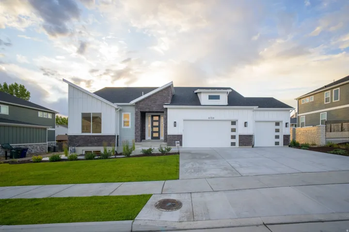 Contemporary exterior featuring a multi-textured facade, a covered entry with a modern door, a well-maintained front lawn, and a wide concrete driveway with two garage doors
