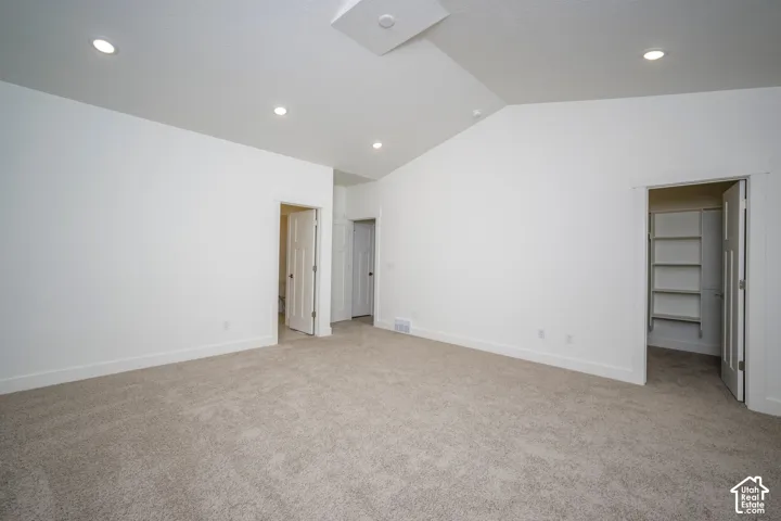 Spacious room featuring vaulted ceilings, recessed lighting, neutral carpeting, and multiple doorways including a walk-in closet with built-in shelving