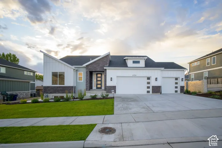 Contemporary exterior featuring a multi-textured facade, a covered entry with a modern door, a well-maintained front lawn, and a wide concrete driveway with two garage doors